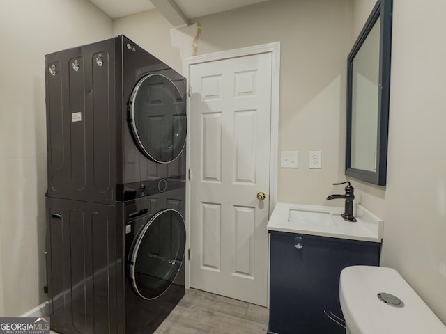 clothes washing area with laundry area, stacked washing maching and dryer, a sink, and light wood-style floors