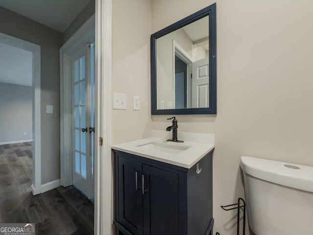 bathroom featuring toilet, baseboards, wood finished floors, and vanity