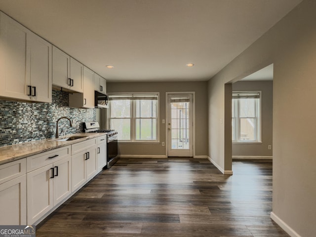 kitchen with stainless steel gas stove, tasteful backsplash, white cabinets, light stone counters, and a sink