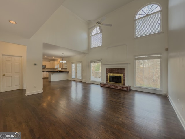 unfurnished living room with a brick fireplace, baseboards, dark wood-style floors, and ceiling fan