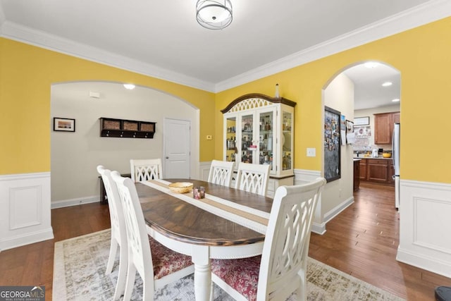 dining area with arched walkways, dark wood-type flooring, wainscoting, and crown molding