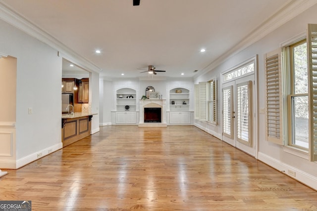 unfurnished living room with built in features, light wood-type flooring, crown molding, and ceiling fan