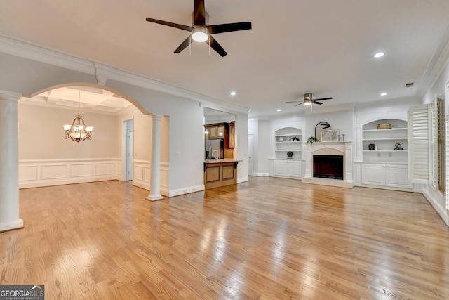 unfurnished living room featuring built in features, light wood-style floors, crown molding, and ornate columns