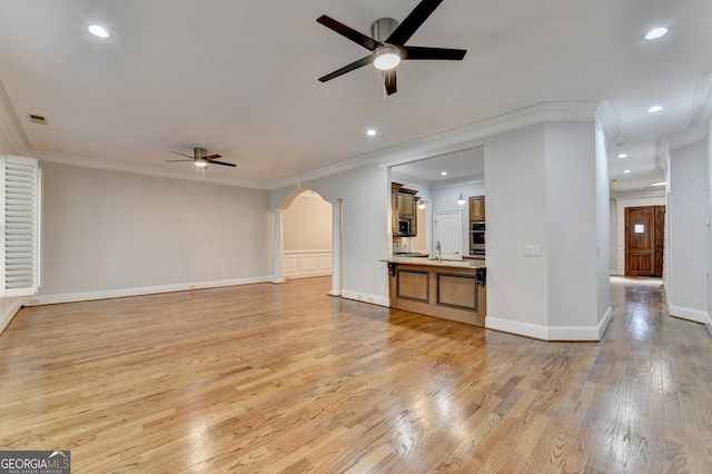 unfurnished living room with crown molding, arched walkways, ceiling fan, and light wood-style flooring