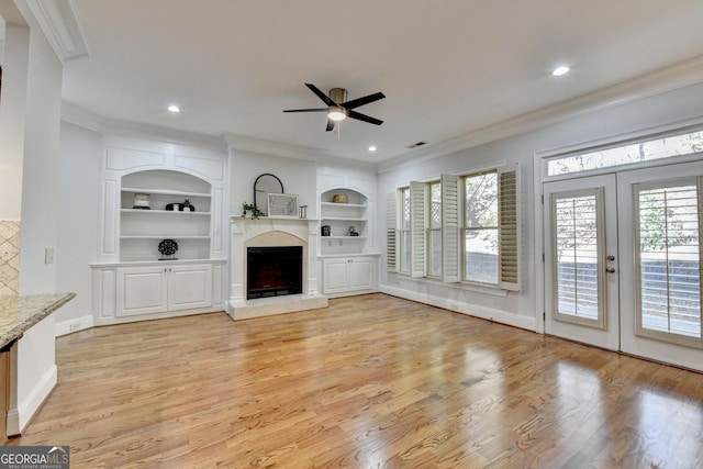 unfurnished living room featuring built in features, a fireplace with raised hearth, visible vents, light wood-style flooring, and ornamental molding