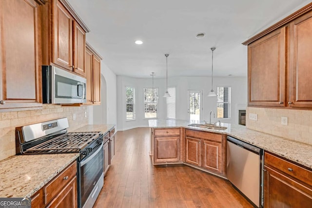 kitchen with light stone counters, dark wood finished floors, appliances with stainless steel finishes, a sink, and a peninsula