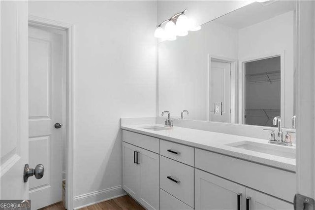 full bath featuring double vanity, baseboards, a sink, and wood finished floors