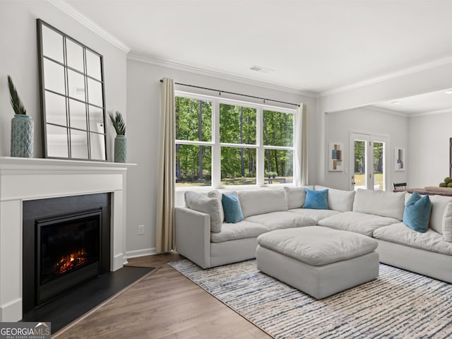 living area with wood finished floors, visible vents, french doors, ornamental molding, and a glass covered fireplace