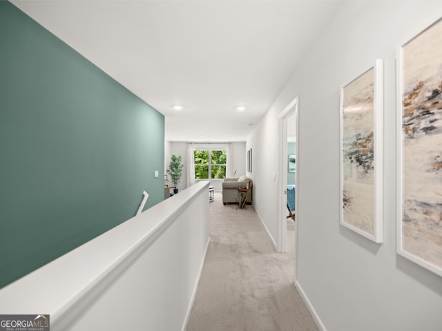 hallway featuring baseboards, an upstairs landing, and light colored carpet