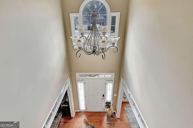 entrance foyer with a chandelier, wood finished floors, a towering ceiling, and baseboards