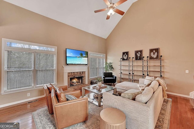 living area featuring baseboards, visible vents, wood finished floors, a fireplace, and high vaulted ceiling