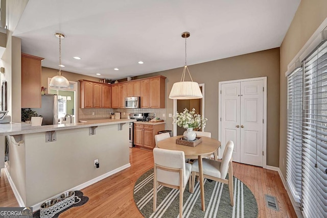 kitchen featuring stainless steel appliances, light countertops, visible vents, light wood-style floors, and a peninsula