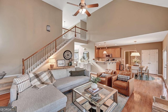 living room featuring light wood finished floors, stairs, baseboards, and a ceiling fan