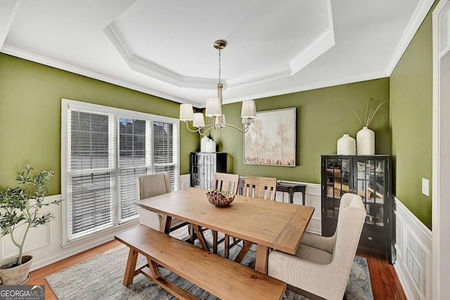 dining space featuring a wainscoted wall, a tray ceiling, wood finished floors, and a notable chandelier