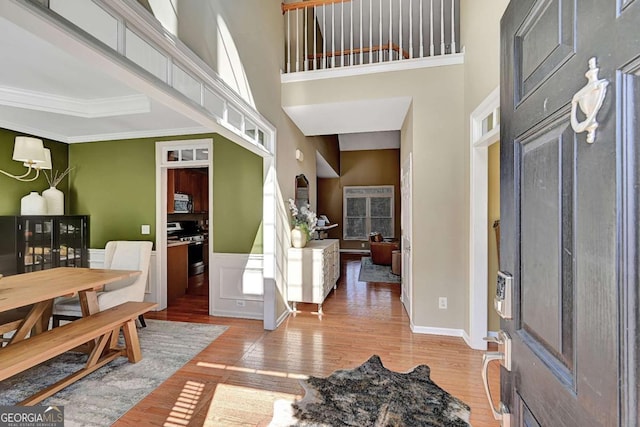 foyer featuring baseboards, wainscoting, a towering ceiling, wood finished floors, and crown molding