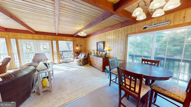 dining area with carpet floors, beam ceiling, a notable chandelier, and wood walls