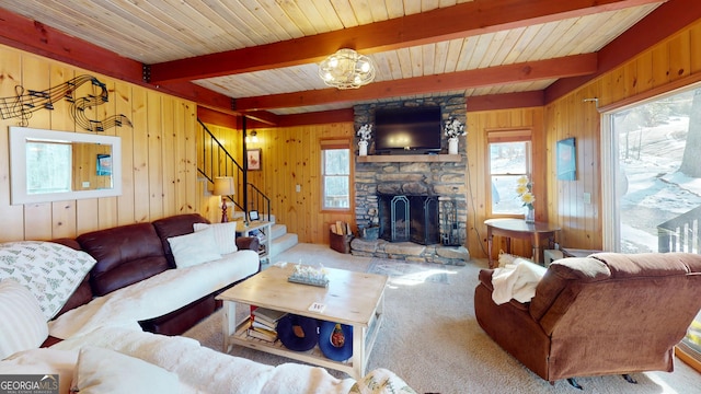 carpeted living area with a fireplace, wood walls, beamed ceiling, and stairs