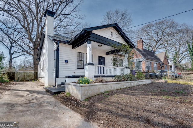 view of front of house featuring a porch, a chimney, and fence