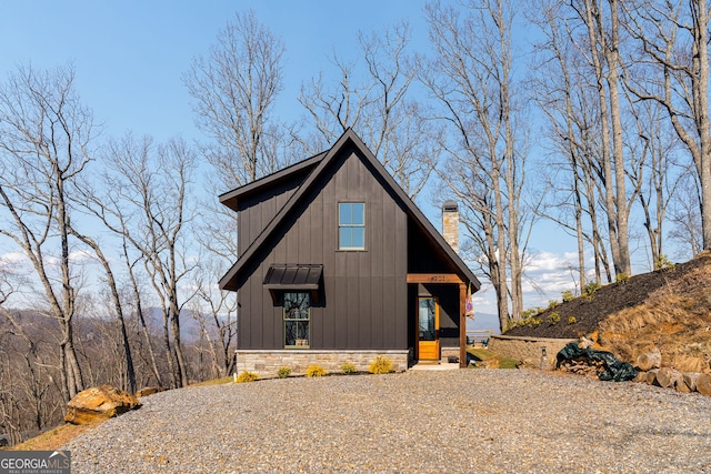 view of front of home featuring stone siding, a chimney, gravel driveway, and board and batten siding