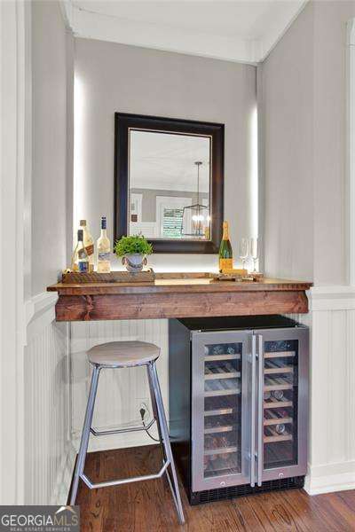 bar featuring a dry bar, beverage cooler, a wainscoted wall, wood finished floors, and a decorative wall