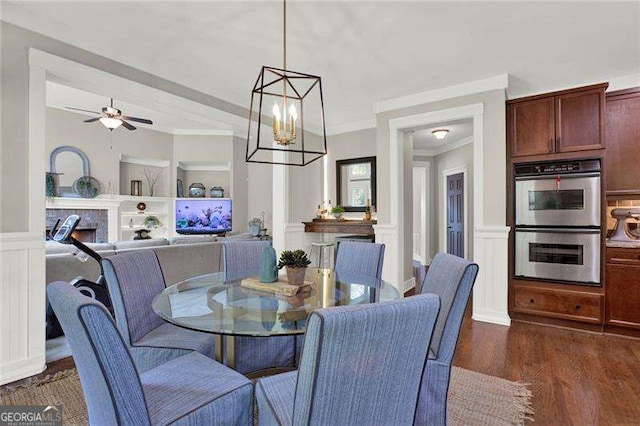 dining space featuring a decorative wall, a wainscoted wall, dark wood-type flooring, a lit fireplace, and ornamental molding