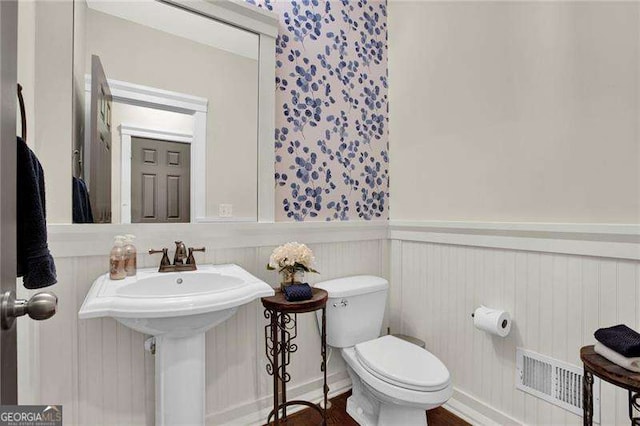 half bath featuring toilet, visible vents, a sink, and wainscoting