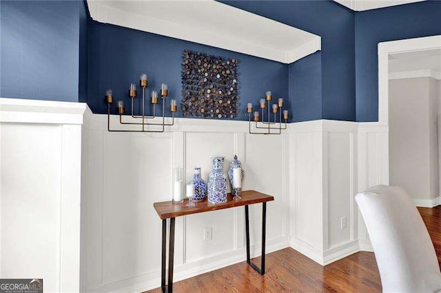 bar featuring a decorative wall, wood finished floors, and wainscoting