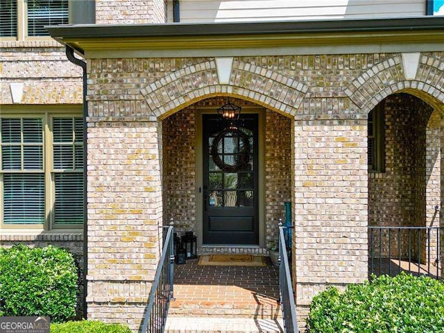 view of exterior entry featuring brick siding and fence