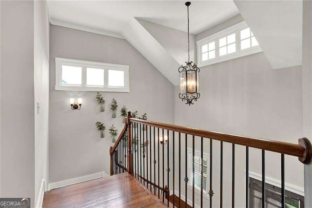 staircase featuring lofted ceiling, plenty of natural light, a chandelier, and wood finished floors