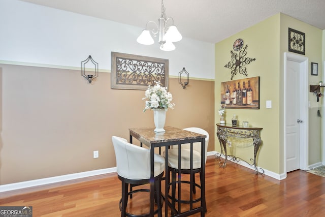 dining space featuring a notable chandelier, a textured ceiling, baseboards, and wood finished floors