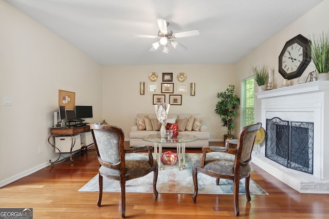 interior space featuring a fireplace with raised hearth, ceiling fan, wood finished floors, and baseboards