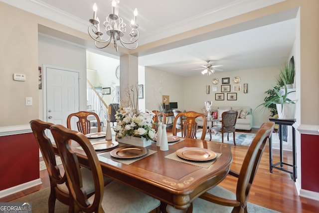 dining area with ceiling fan with notable chandelier, wood finished floors, baseboards, stairway, and crown molding