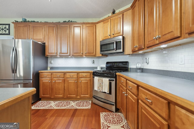 kitchen featuring dark wood-style floors, stainless steel appliances, brown cabinetry, and backsplash