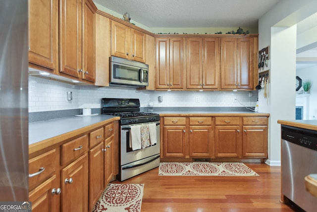 kitchen featuring stainless steel appliances, brown cabinetry, light wood finished floors, and tasteful backsplash