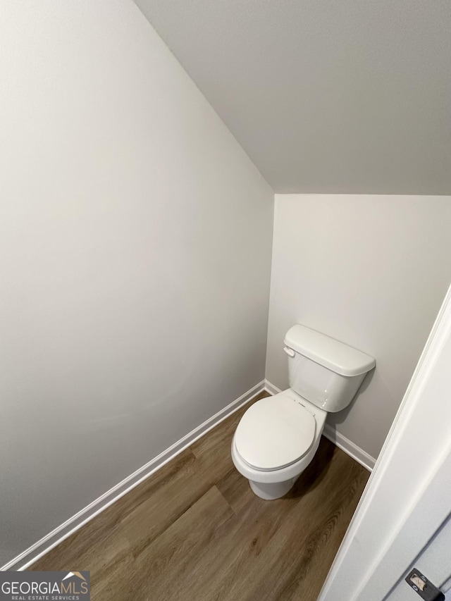 bathroom with toilet, baseboards, vaulted ceiling, and wood finished floors