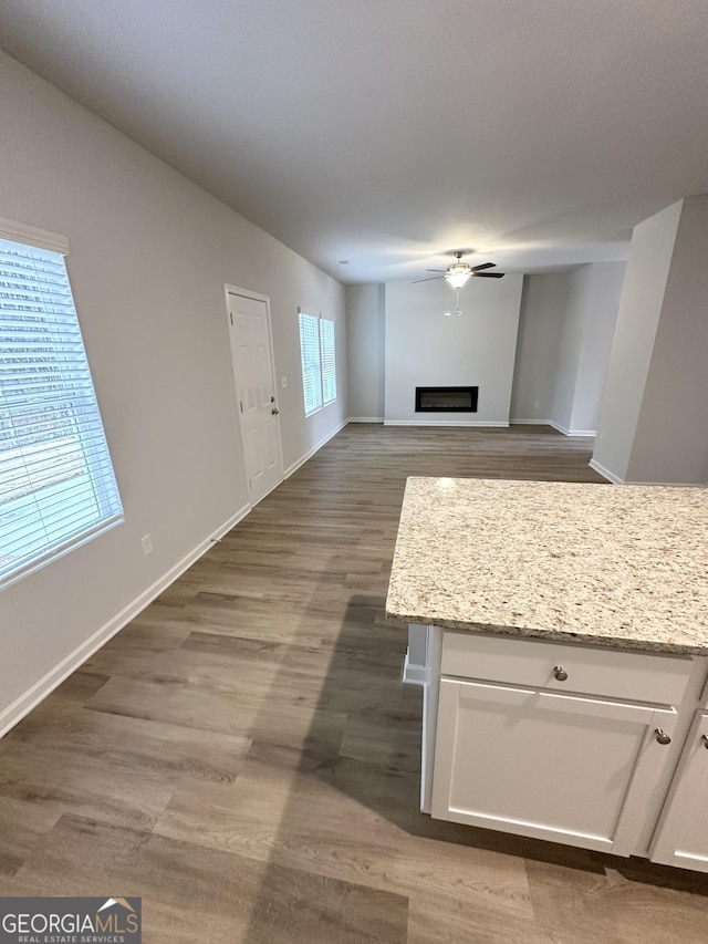 kitchen featuring baseboards, a ceiling fan, wood finished floors, a fireplace, and white cabinetry