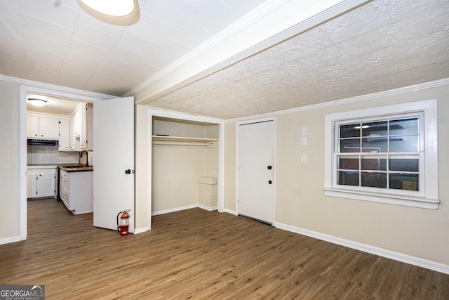 unfurnished bedroom with baseboards, ornamental molding, wood finished floors, a textured ceiling, and a sink