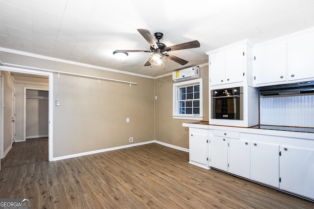 kitchen with a wall unit AC, white cabinets, wood finished floors, and oven