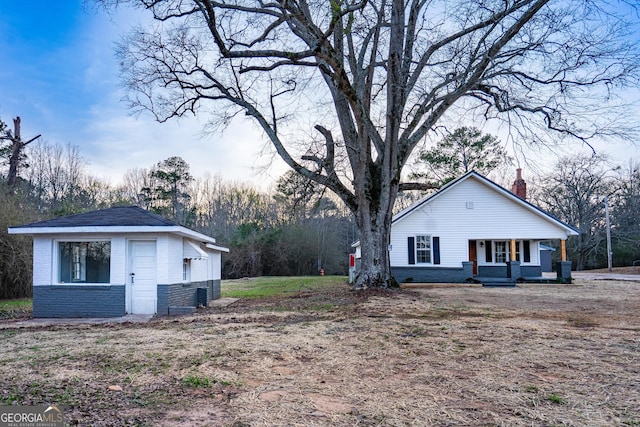 view of side of property with covered porch, a chimney, an outbuilding, and brick siding