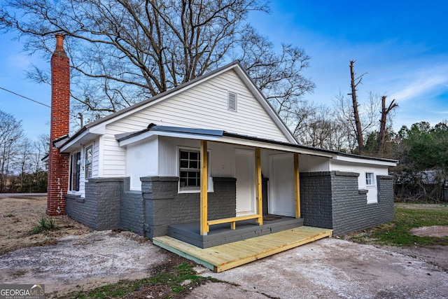 view of front of home featuring covered porch, stone siding, and a chimney