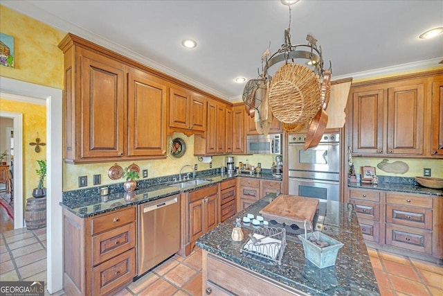 kitchen with brown cabinetry, dark stone counters, an inviting chandelier, stainless steel appliances, and a sink