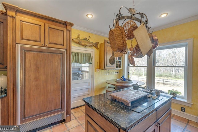 kitchen featuring ornamental molding, a wealth of natural light, brown cabinets, and dark stone countertops