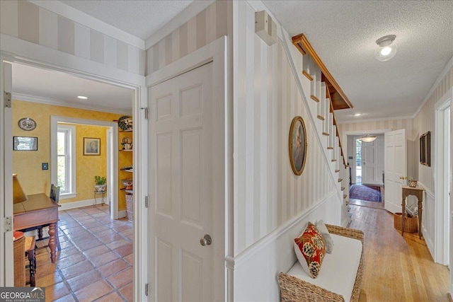 corridor featuring stairs, crown molding, a textured ceiling, and wallpapered walls