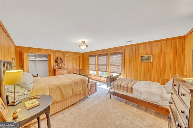 bedroom with light colored carpet, visible vents, and wooden walls