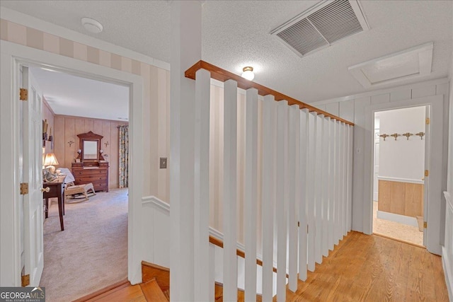 corridor featuring a textured ceiling, light wood finished floors, visible vents, and attic access