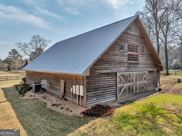 view of barn featuring fence, a lawn, and central AC unit