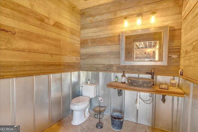 half bathroom featuring toilet, wooden walls, and a sink