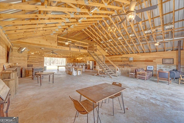 interior space with a ceiling fan, a wood stove, visible vents, and high vaulted ceiling