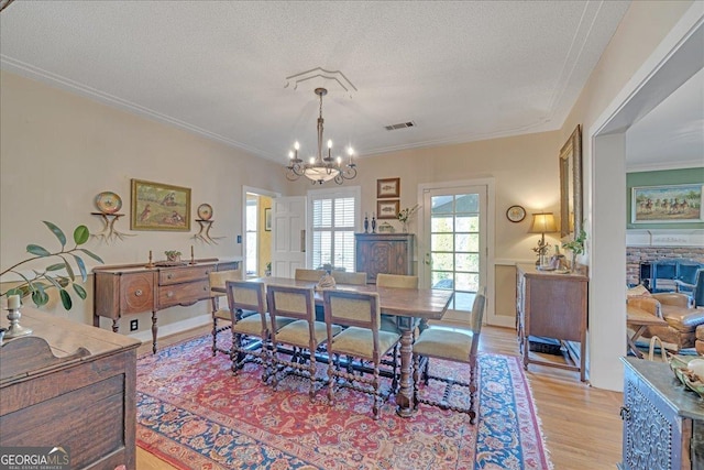 dining space featuring crown molding, a fireplace, light wood finished floors, visible vents, and a textured ceiling