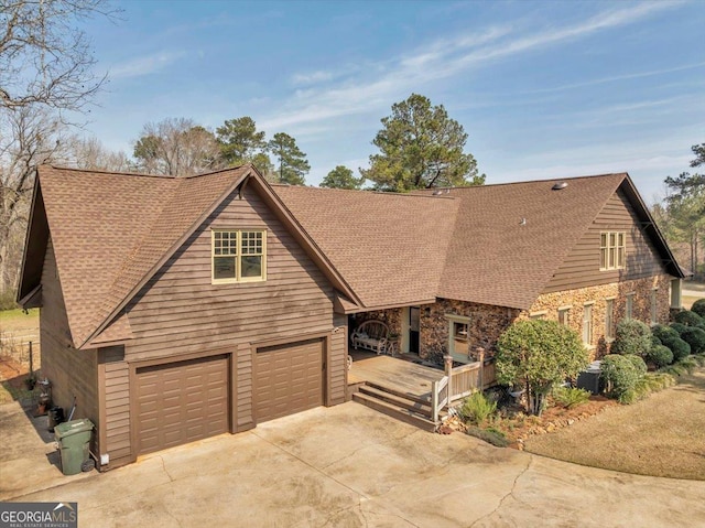 chalet / cabin featuring a garage, central air condition unit, concrete driveway, and roof with shingles